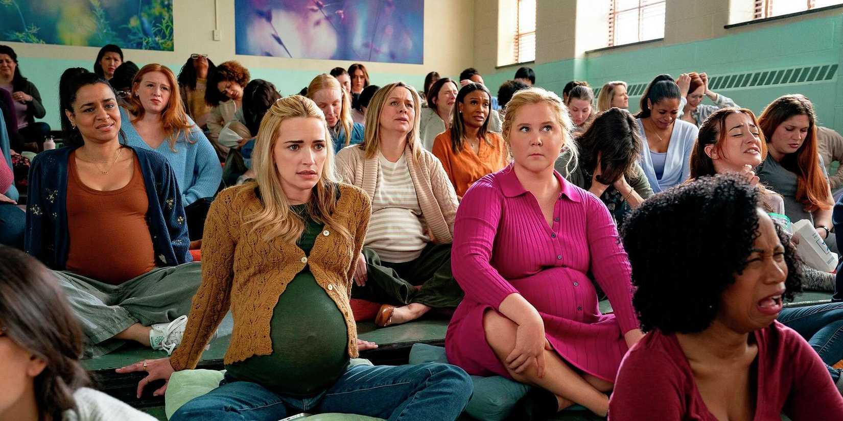 Brianne Howey and Amy Schumer sitting among pregnant women at a support group in Kinda Pregnant
