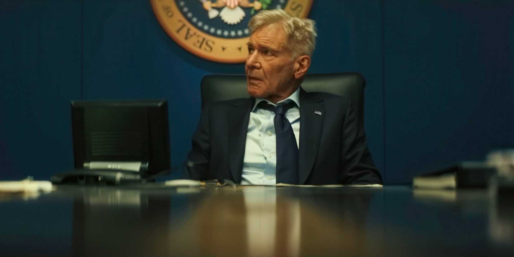 Harrison Ford as President Thaddeus Ross sitting behind a table in Captain America Brave New World