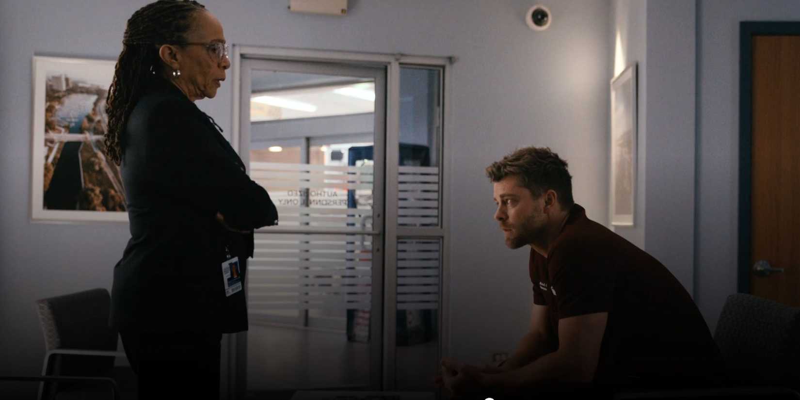 Chicago Med Sharon standing with her arms crossed looking at Mitch who is sitting with his head bowed