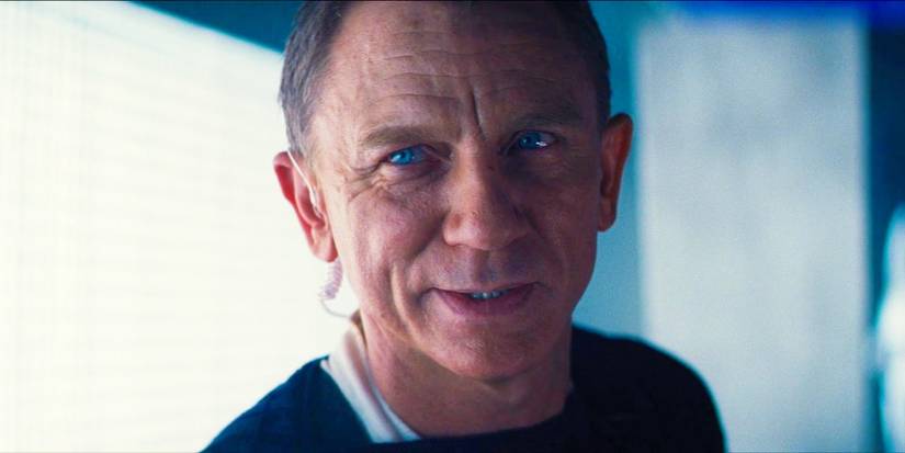Daniel Craig as James Bond leaning forward with a slight smile in No Time to Die