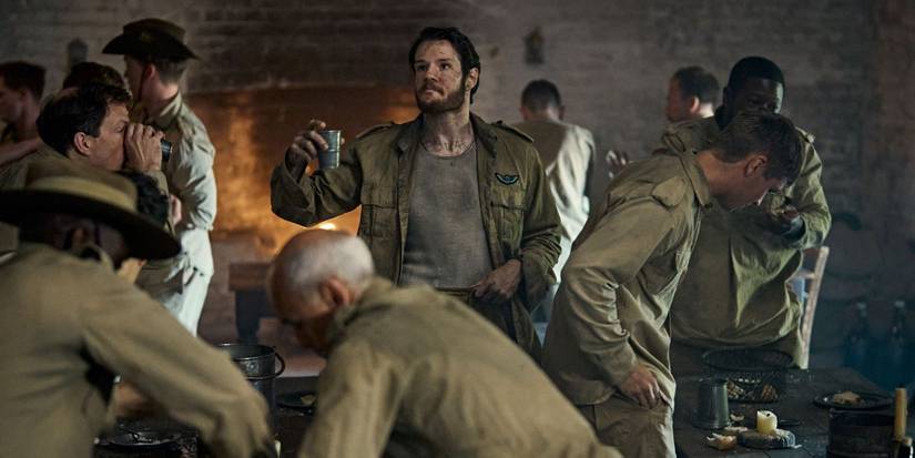 David Stirling (Connor Swindells) holding up a cup in a POW camp surrounded by soldiers in SAS Rogue Heroes.