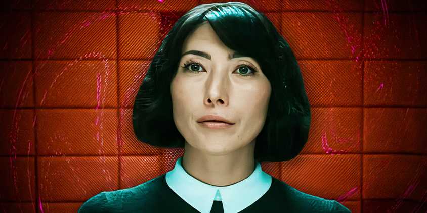 Dichen Lachman as Ms. Casey looking pensive in Severance season 1 (2022) above a red background of Lumon's offices