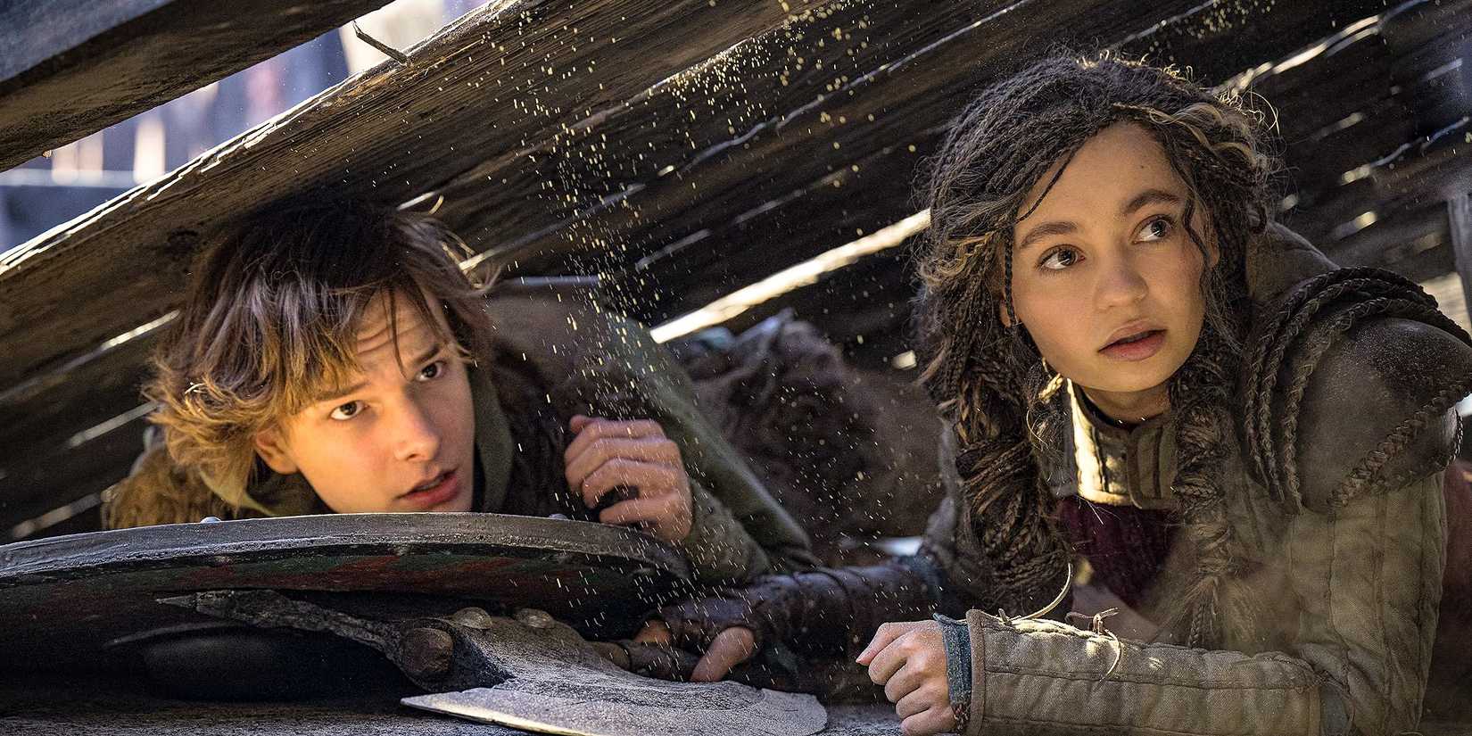 Hiccup (Mason Thames) and Astrid (Nico Parker) hiding under some planks in How To Train Your Dragon (2025)