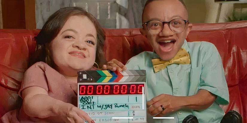 jay & Pamela with the couple holding a clapperboard smiling while seated on a coach.