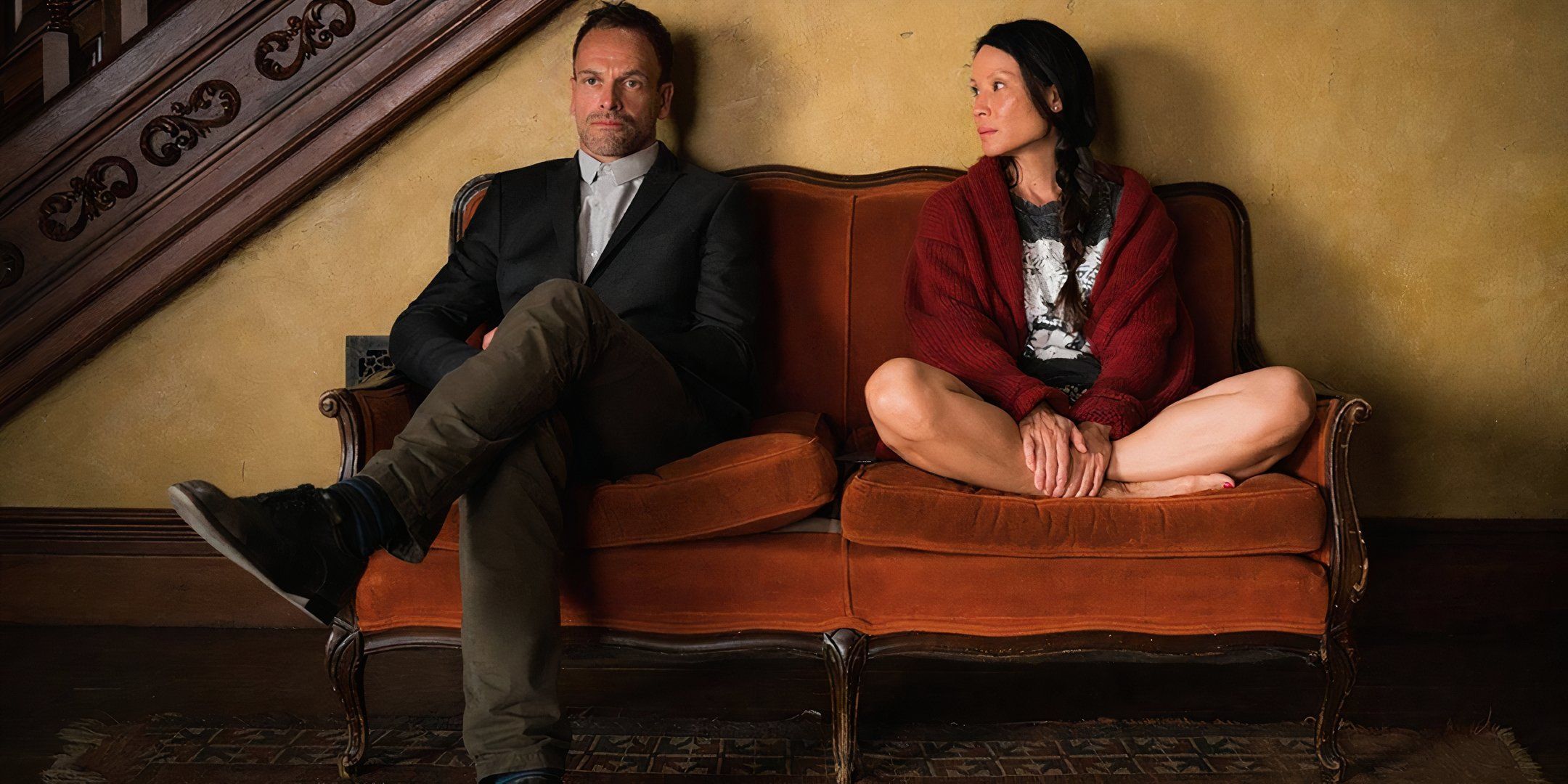 Jonny Lee Miller's Sherlock and Lucy Liu's Joan sitting on a couch with each other in Elementary