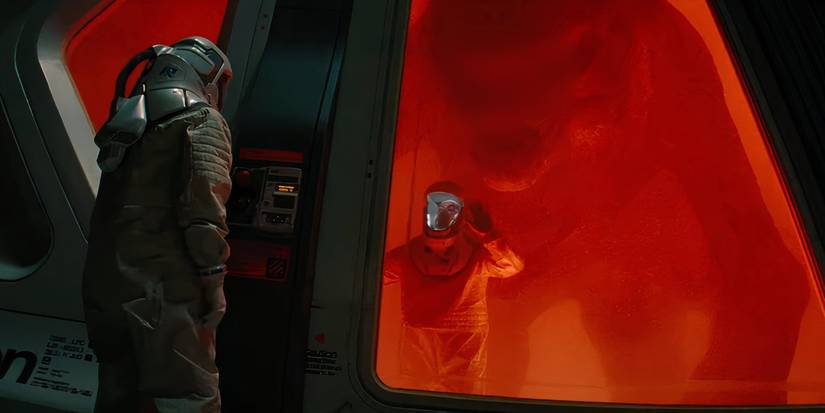 A man in an air-tight suit looks on as another man is trapped inside a glass enclosure with a monstrous dinosaur in Jurassic World Rebirth