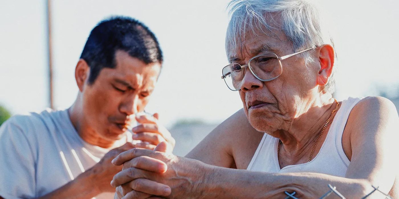 Long Ma (Hiep Tran Nghia) leaning on a fence as Tay Du'o'ng smokes a cigarette in The Accidental Getaway Driver.