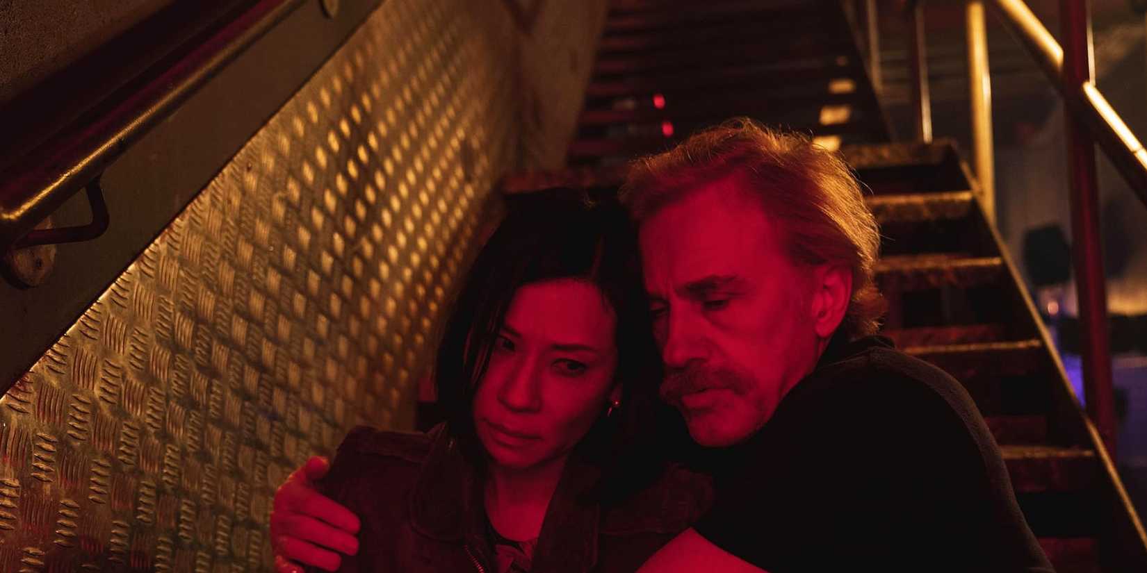 Lucy Liu and Christoph Waltz in Old Guy emabracing while sitting on a staircase 