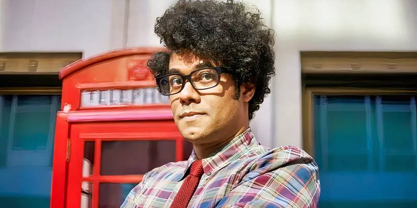 Maurice with his arms folded in front of an English telephone booth in The IT Crowd