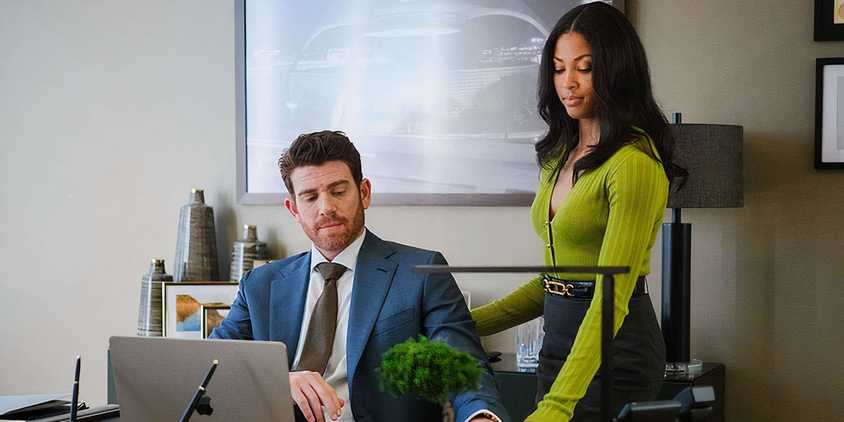 Lex Scott Davis as Erica Rollins standing above Bryan Greenberg as Rick Dodsen at his desk in Suits LA