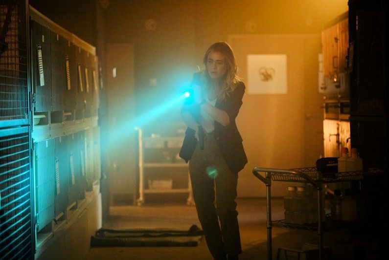 The Hunting Party's Bex in a dark room with animal cages holding a flashlight.