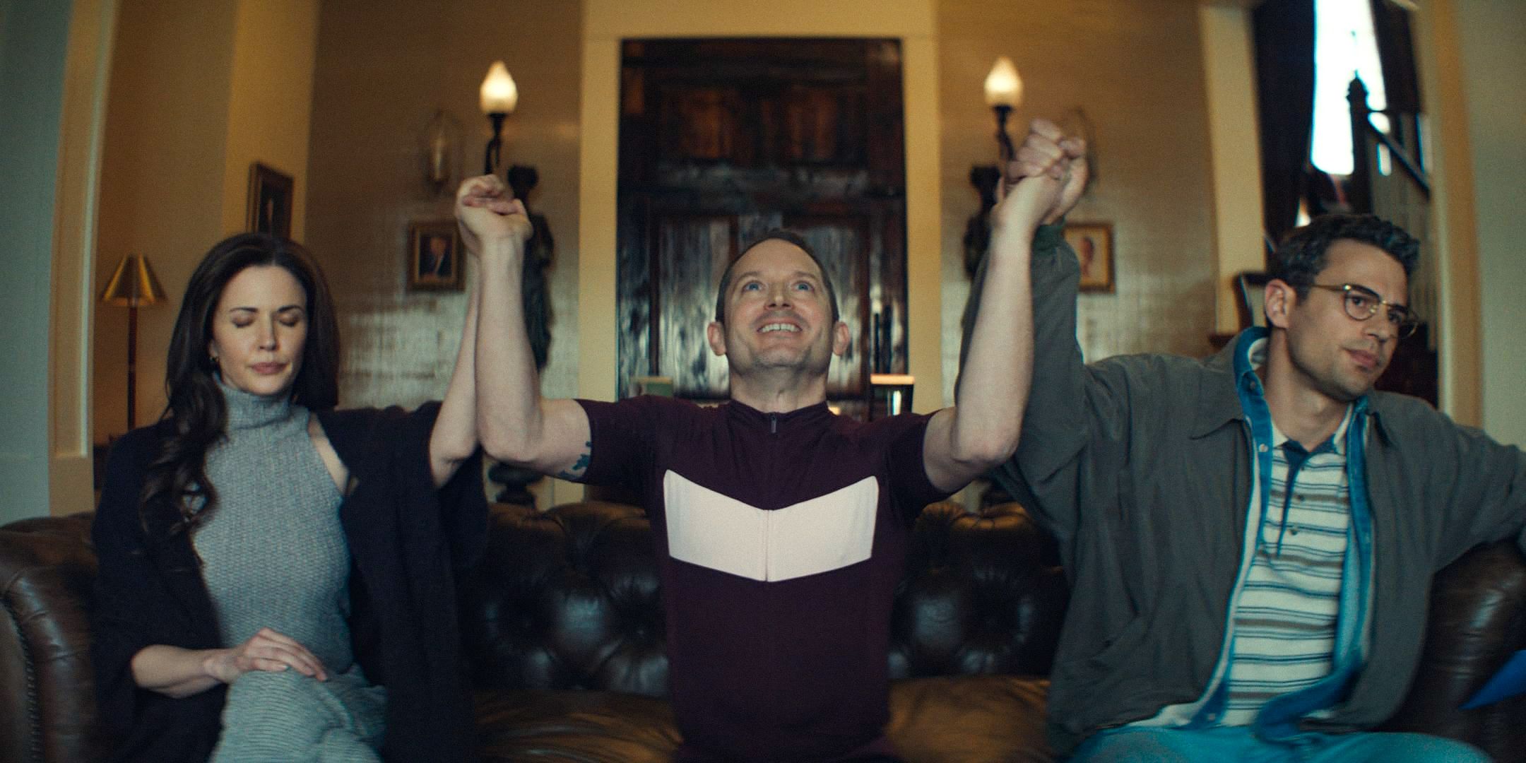 Petey's Mom (Laura Mennell), Ted (Elijah Wood), and Hal (Theo James) praying and raising their hands in the air in The Monkey