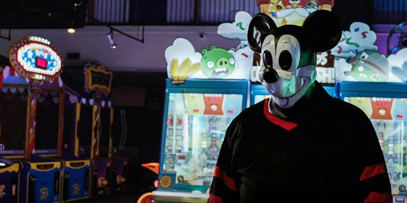 The Mouse Trap still killer wearing Mickey mask in front of claw games