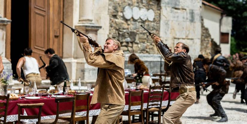 Two SAS soldiers shooting into the air during an outdoor dinner in SAS Rogue Heroes.