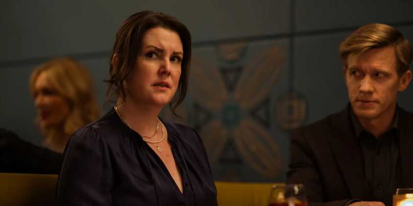 Adult Shauna (Melanie Lynskey) sitting next to Jeff (Warren Kole) and looking concerned in Yellowjackets season 3