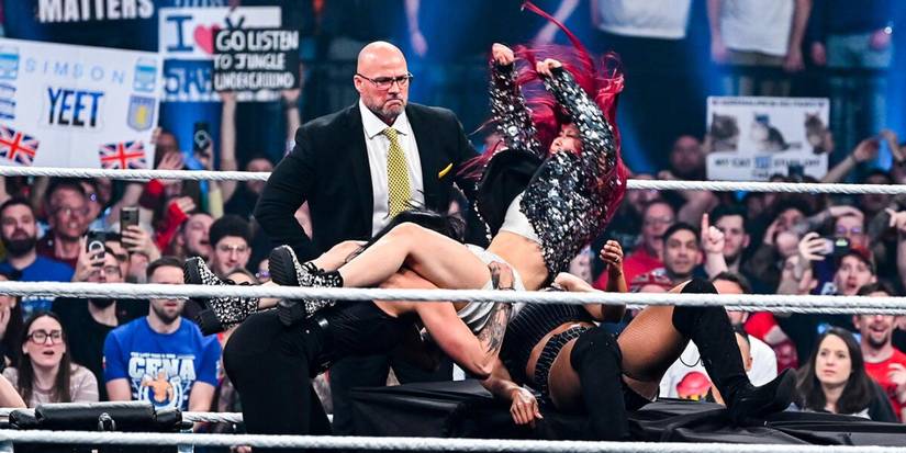 Adam Pearce watches Iyo Sky get powerbombed by Rhea Ripley onto Biance Belair on a table on WWE Monday Night Raw