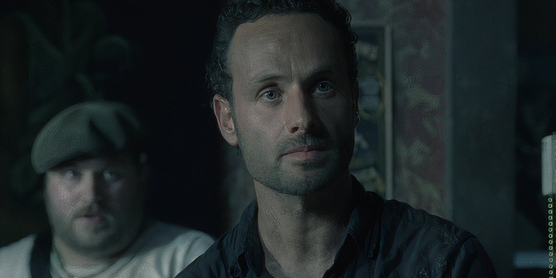 Andrew Lincoln as Rick Grimes looking serious inside a bar with a stranger behind him in The Walking Dead