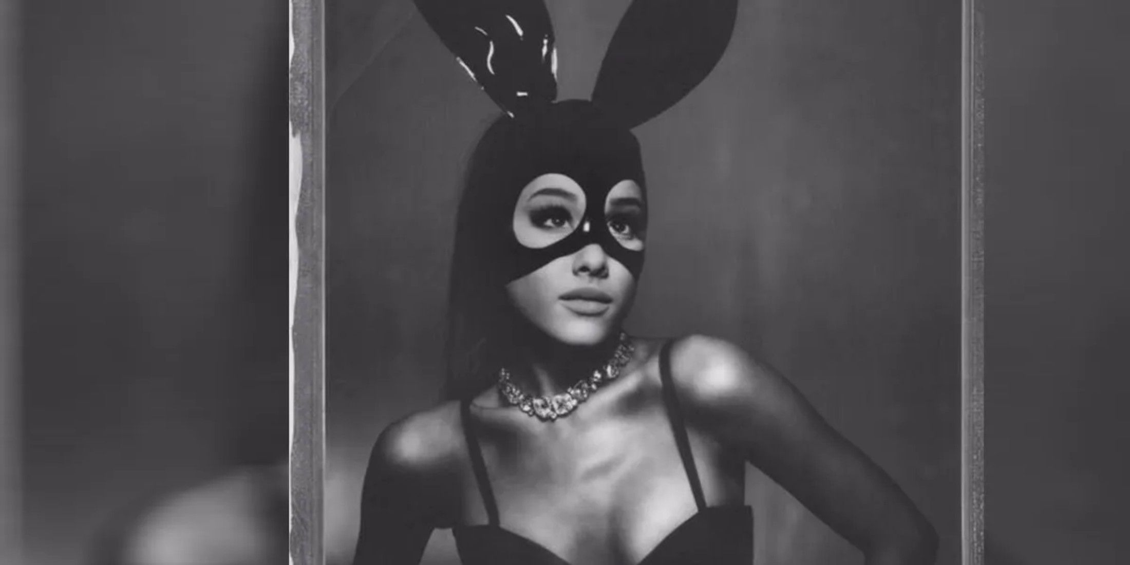 The photo is in black and white, Arianna has on a black dress and a necklace. She wears a mask with bunny ears that covers the top part of her head, but her eyes and eyebrows are visible.