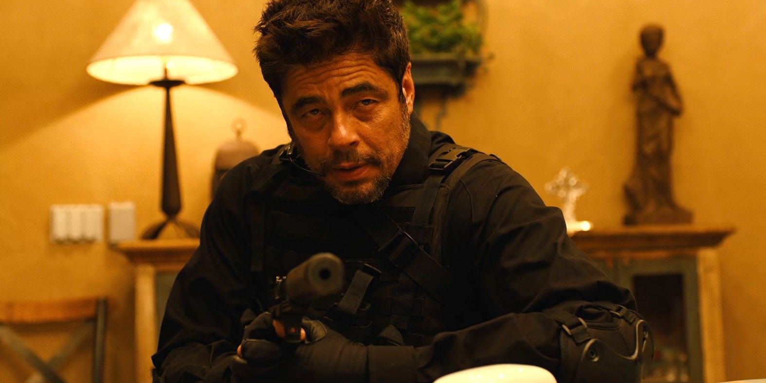 Benicio del Toro as Alejandro holding a silenced pistol and wearing a stealth suit in Sicario