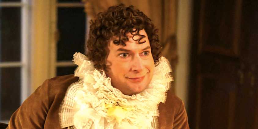 Brandon Scott James' Isaac smiles wearing a huge ruffle in Ghosts season 4 episode 14
