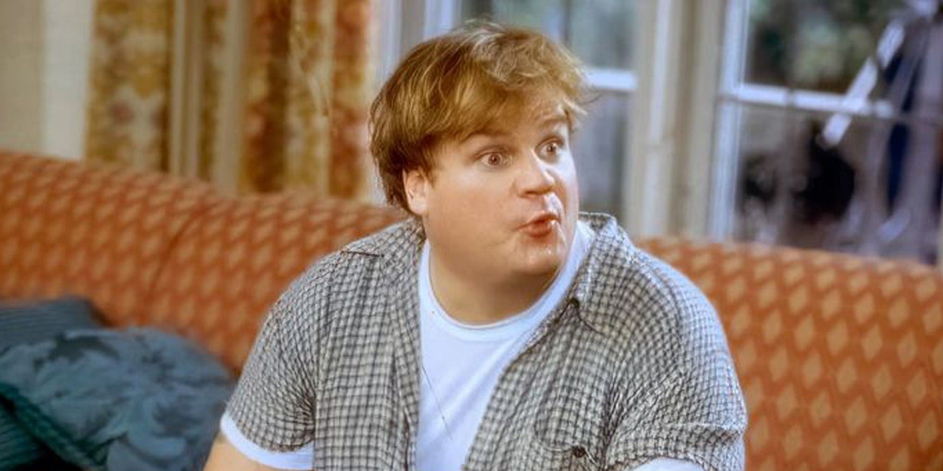 Chris Farley sitting on a couch and making a silly surprised face