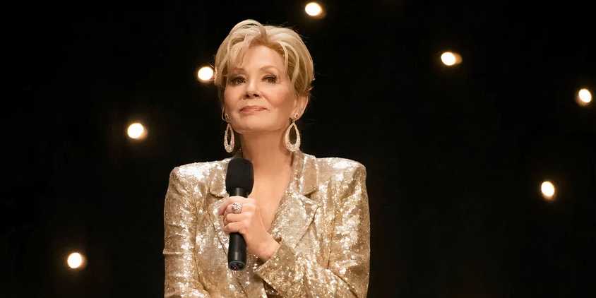 Deborah Vance (Jean Smart) onstage in a gold blazer, holding a microphone in Hacks
