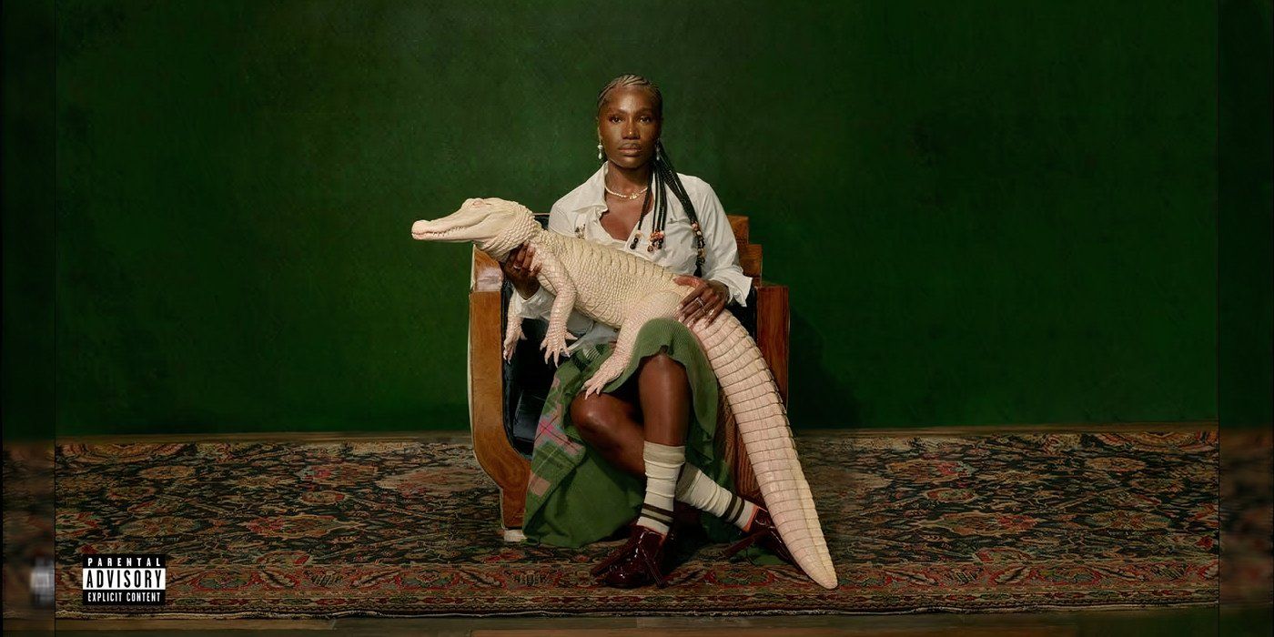 This album cover features a woman holding a white alligator against a green background while sitting in a chair on a carpeted floor. She&rsquo;s wearing a green dress with a white shirt, white socks, and dark shoes.