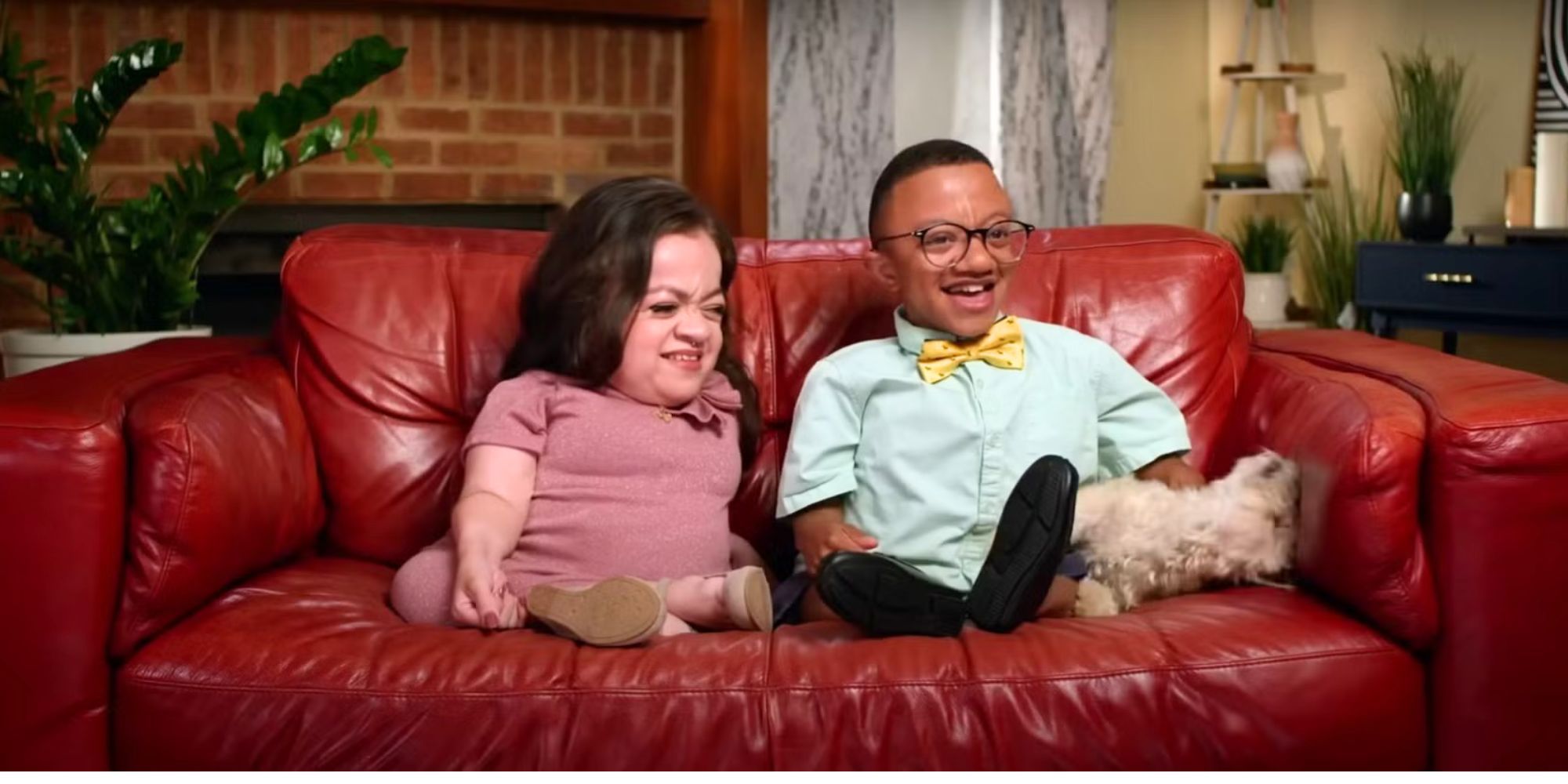 Jay & Pamela Jay Manuel & Pamel Chavez sitting on a couch laughing with their dog Cheddar