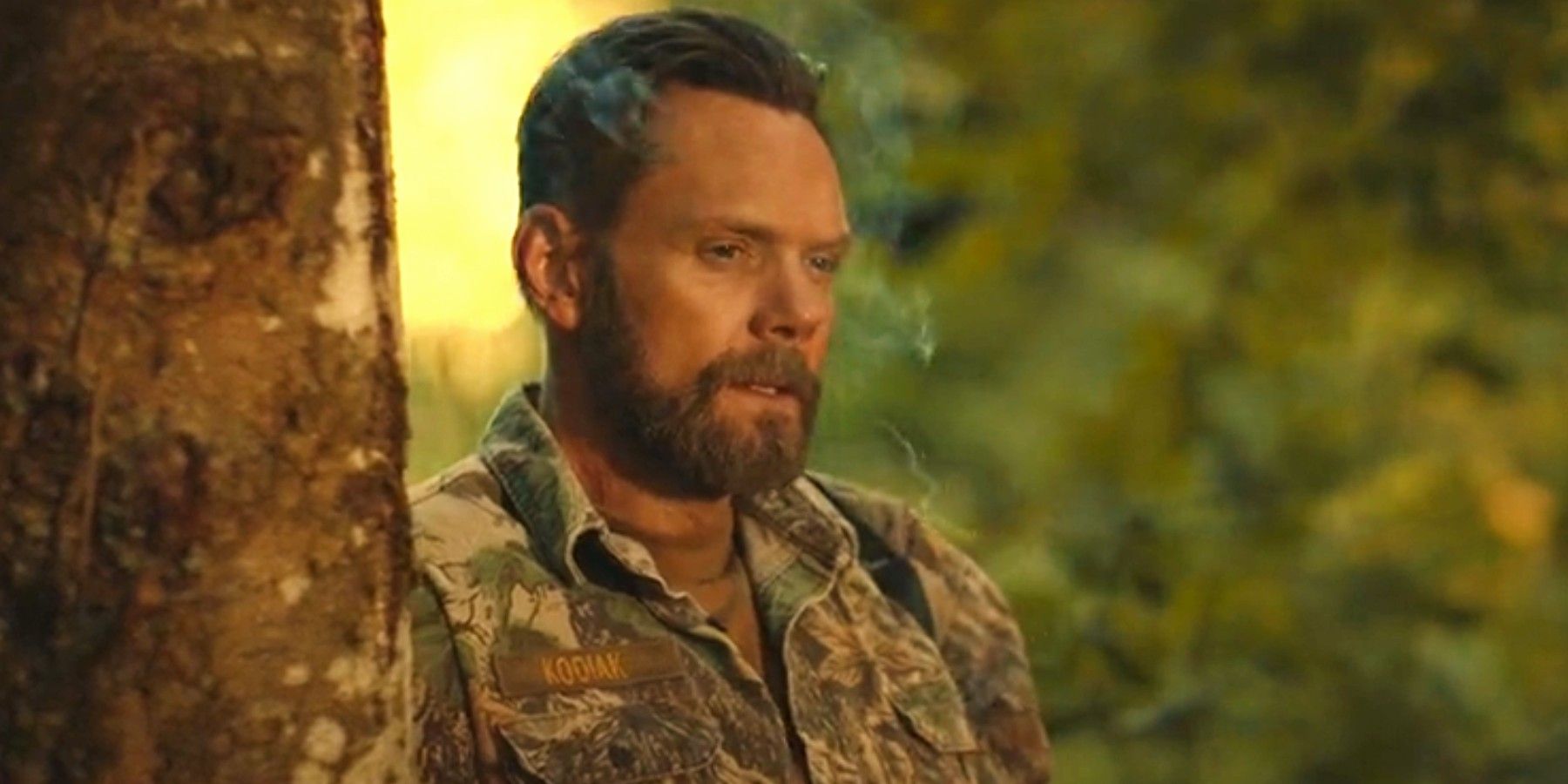 Joel McHale as Kodiak smoking next to a tree in Yellowjackets season 3 episode 7