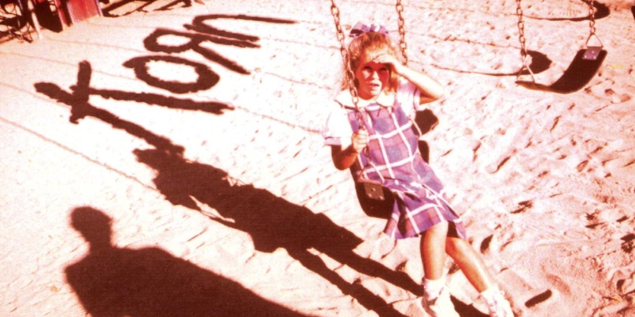There is a girl on a swing, she has on a plaid dress, shoes, and has a bow in her long blond hair. Under her is sand and in the right corner is the word Korn.