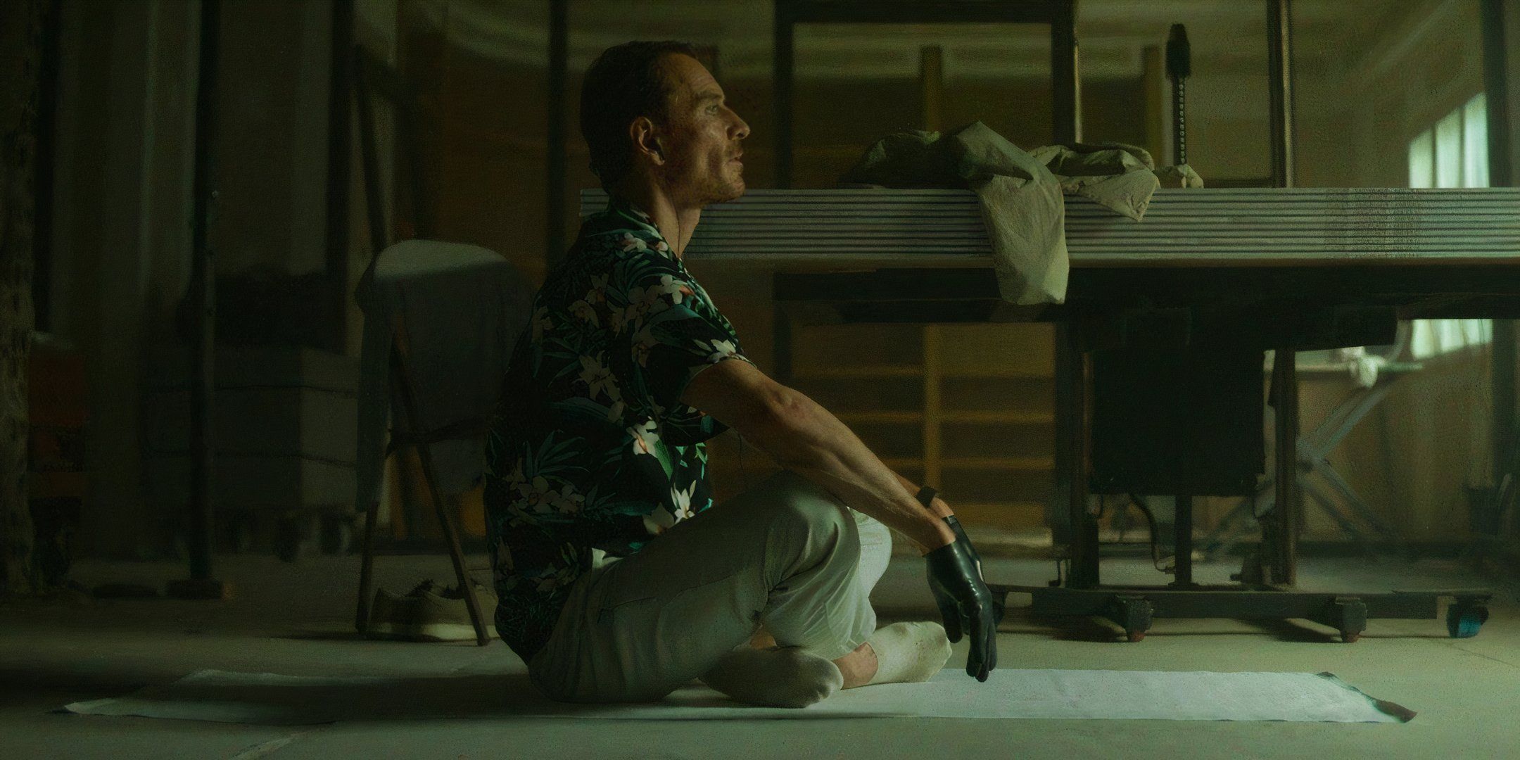 Michael Fᴀssbender sitting on the floor with gloves on in The Killer