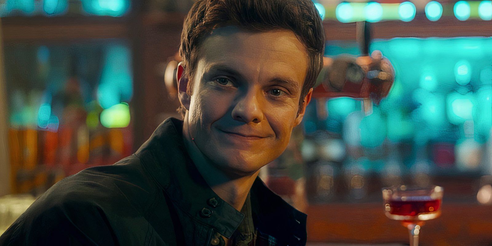 Jack Quaid as Nathan Caine smiles in a bar in Novocaine