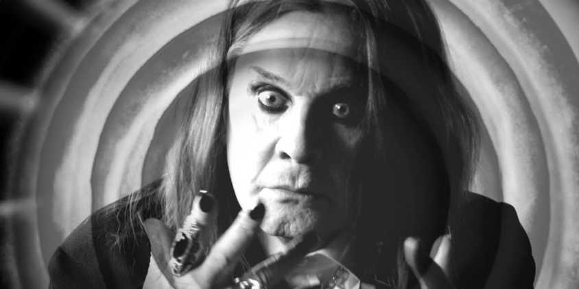 Ozzy Osbourne has long hair, he holds up his hand that has painted nails and rings on his pointer finger and ring finger. The photo is i black and white, with swirls around Ozzy.