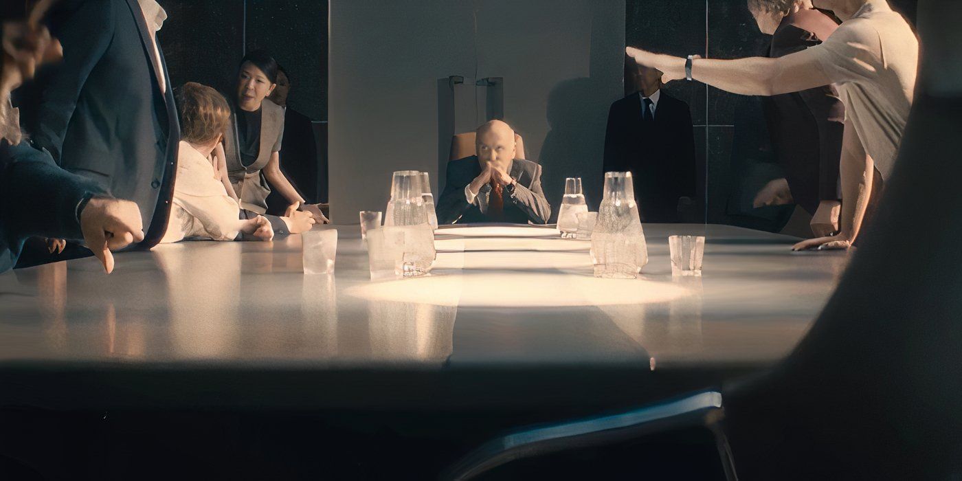 Baines sits thoughtfully at the head of a long table as a meeting goes on around him in Paradise
