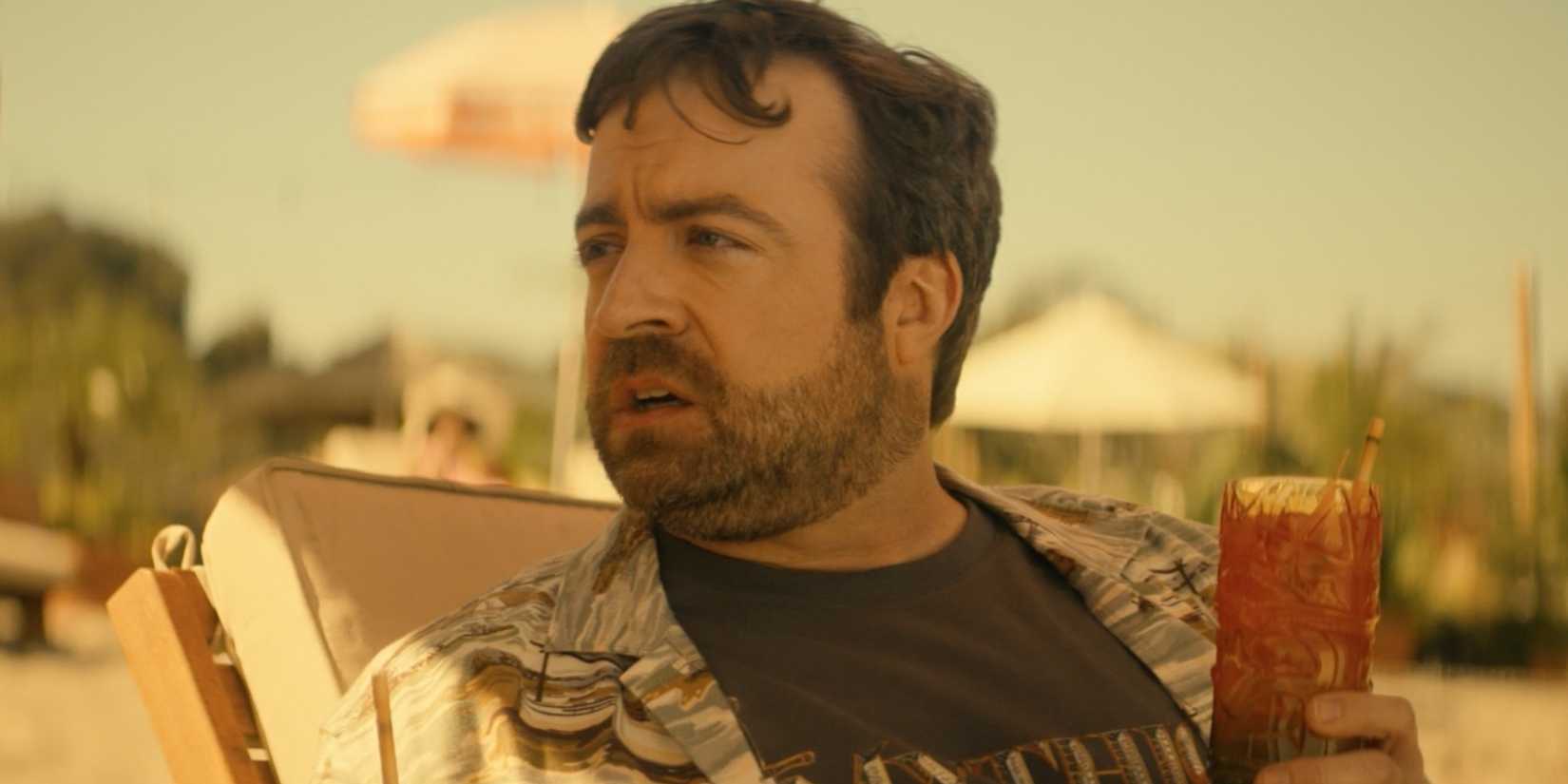 Phil in Side Quest holding a drink on the beach 