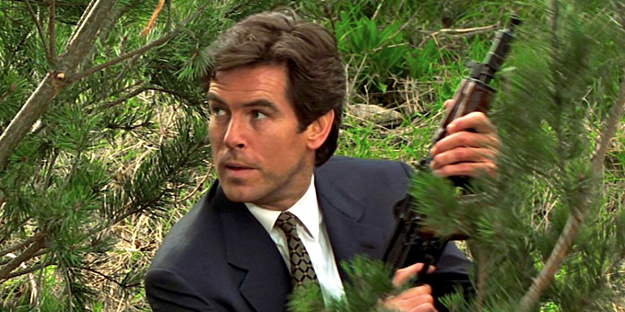 Pierce Brosnan's James Bond crouches among tree branches holding a gun in Goldeneye