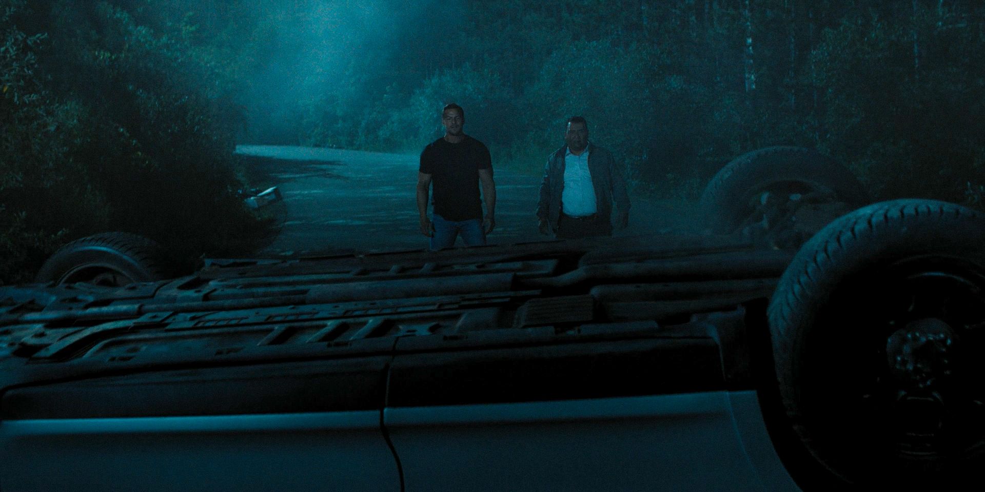 Reacher (Alan Ritchson) and Villanueva (Roberto Montesinos) standing in front of a tipped car in Reacher season 3
