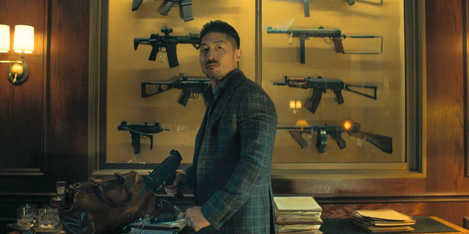 Quinn (Brian Tee) with a display case of assault rifles behind him in Reacher Season 3 Ep 8