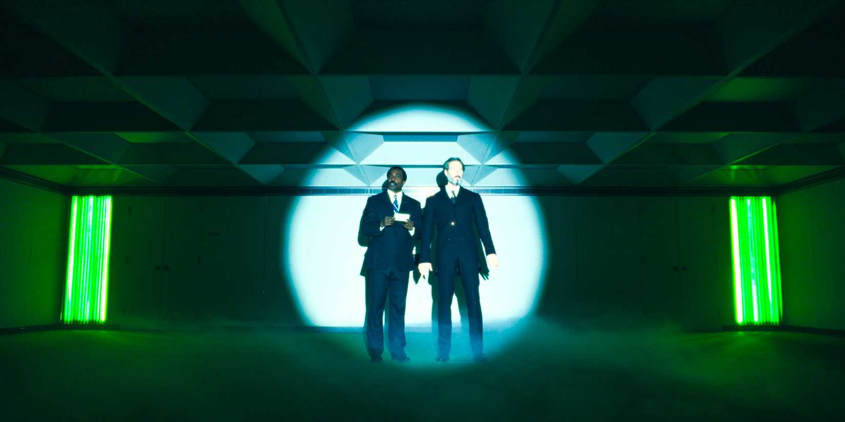 Milchick (Tramell Tillman) standing next to a wax figure of Jame Eagan, hosting Mark's celebration in Severance Season 2 Ep 10
