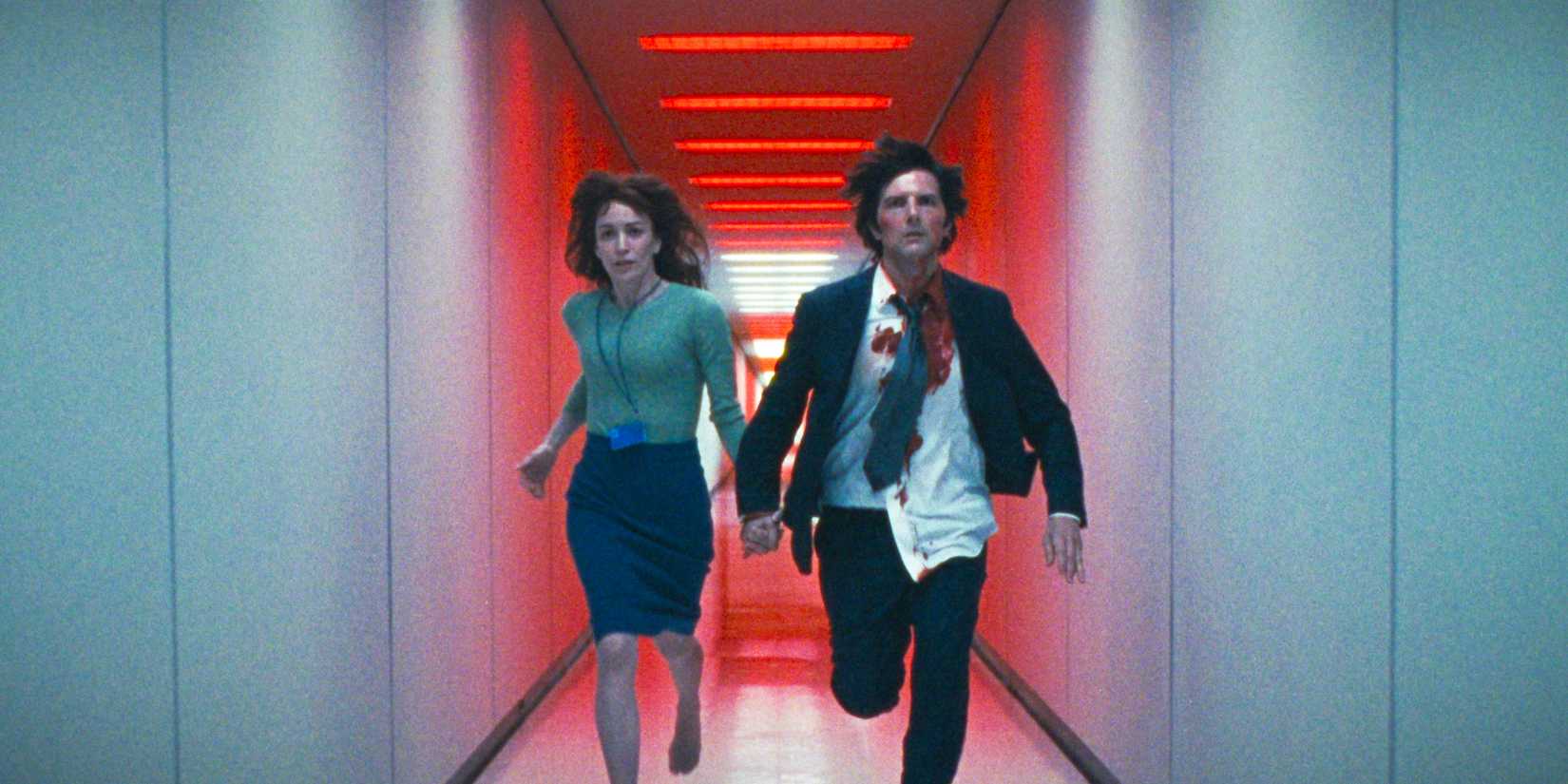 Helly (Britt Lower) and Mark S. (Adam Scott) running hand in hand through a hallway bathed in red light in Severance Season 2 Ep 10