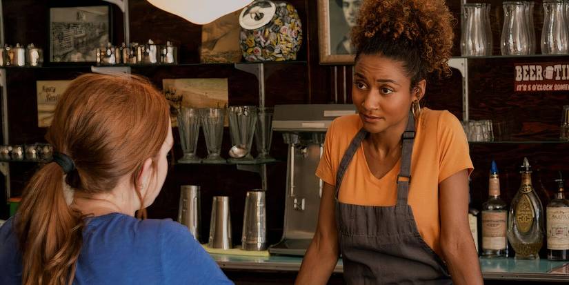 Sydney listens to Maggie with an inquisitive look while standing behind the counter in Sullivan's Crossing