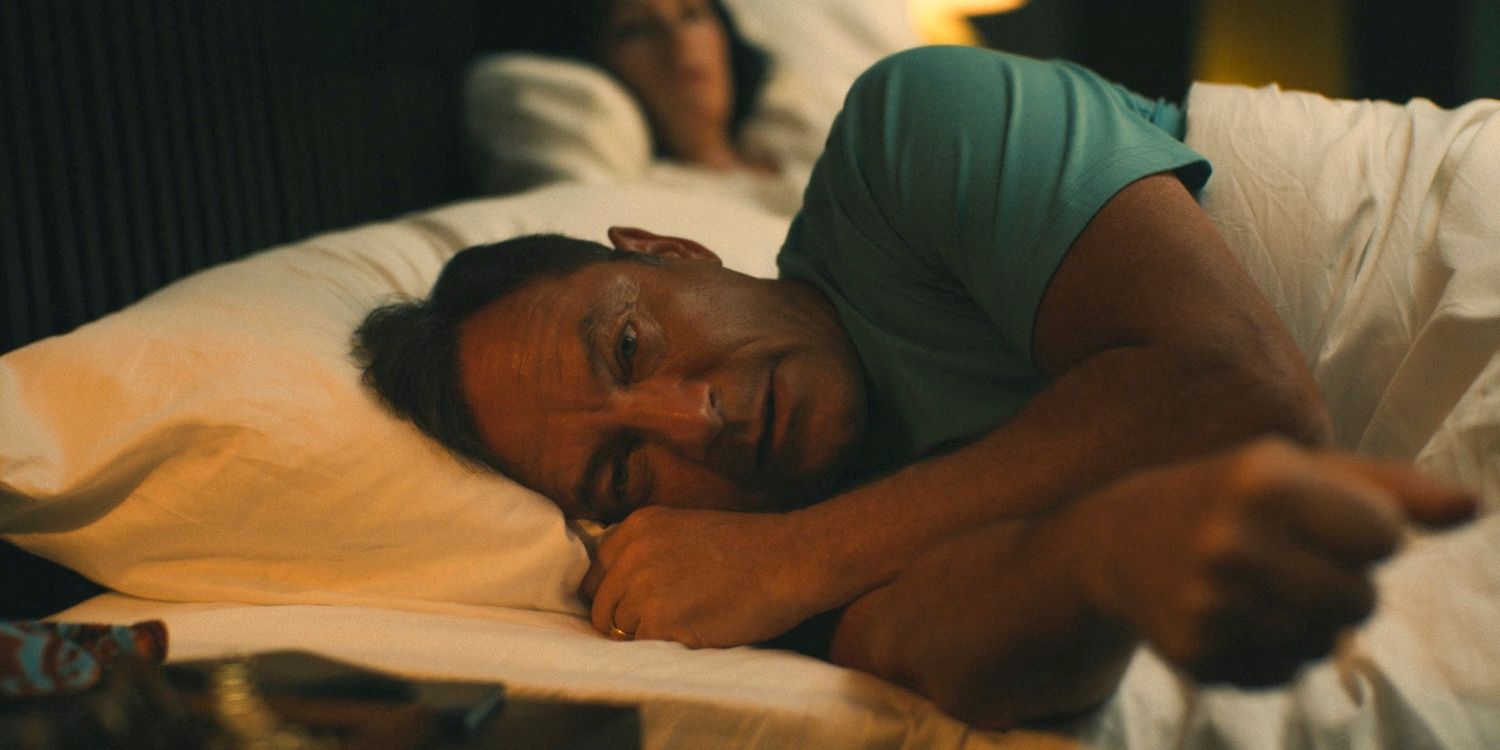 Timothy Ratliff (Jason Isaacs) lying on the bed, looking stressed and thoughtful in The White Lotus Season 3 Ep 3