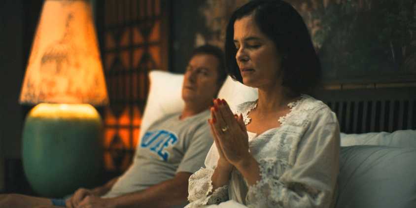Victoria (Parker Posey) praying before bed while Timothy (Jason Isaacs) watches her in The White Lotus Season 3 Ep 7