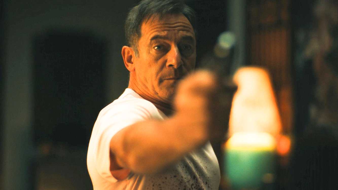The White Lotus Season 3 Episode 7, Timothy Ratliff in a blood-splattered white shirt pointing a gun.
