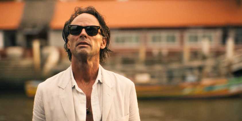 Rick (Walton Goggins), wearing sunglasses and a white suit, arrives at Sritala's house in The White Lotus Season 3 Episode 6 
