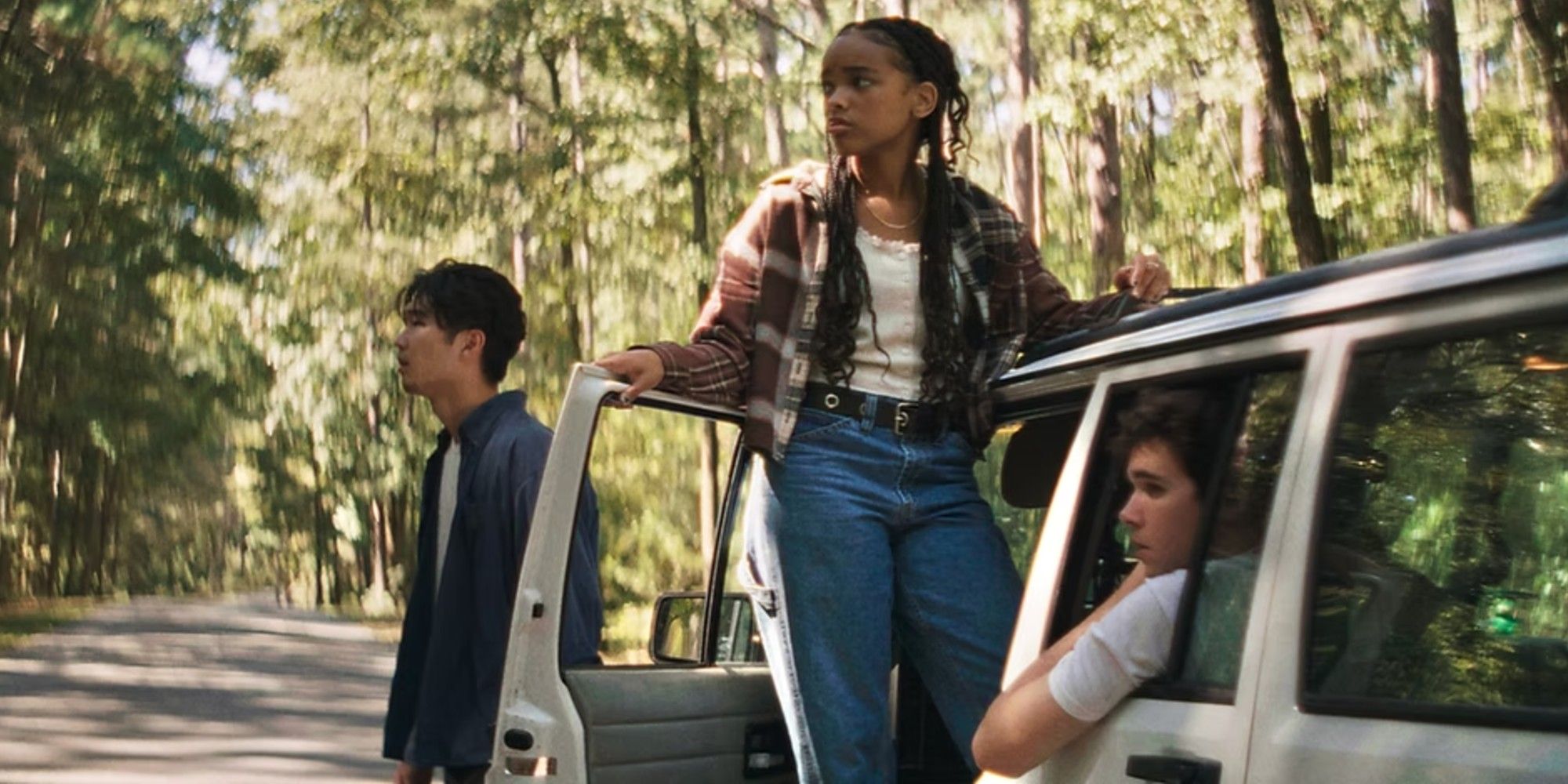 Three friends stand outside their car looking out of frame into the woods