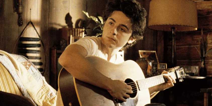 Timothee Chalamet playing guitar as Bob Dylan in A Complete Unknown