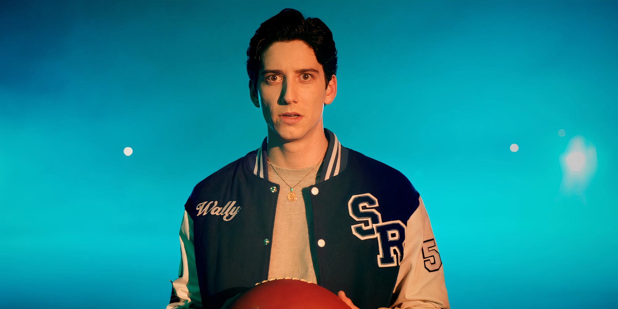 Milo Manheim as Wally holding a football on the field in his scar in School Spirits season 2