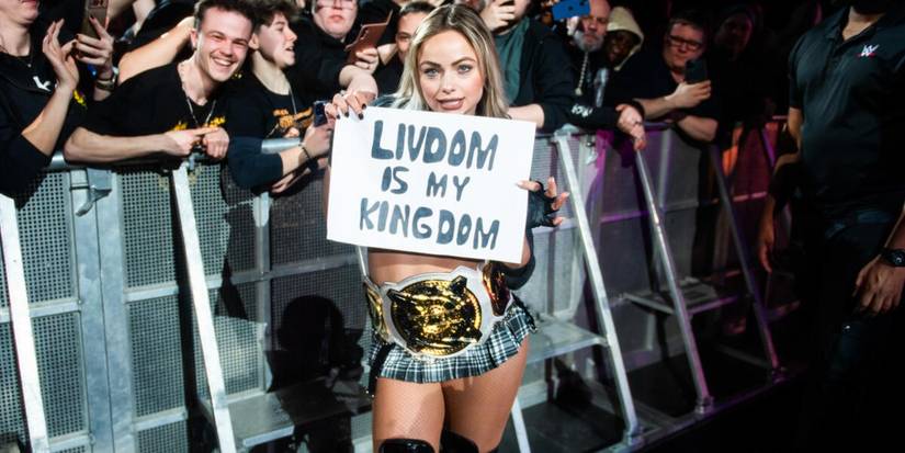 WWE Women's Tag Team Champion Liv Morgan holds up a fan sign at a live event