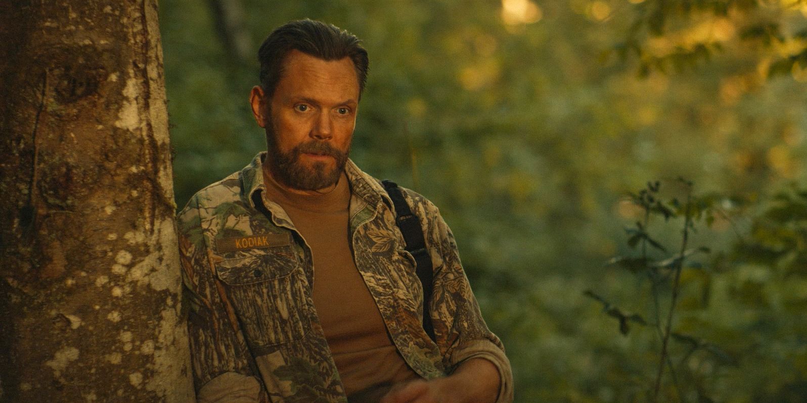 Kodi (Joel McHale) looking thoughtful, leaning against a tree in Yellowjackets Season 3 Episode 7